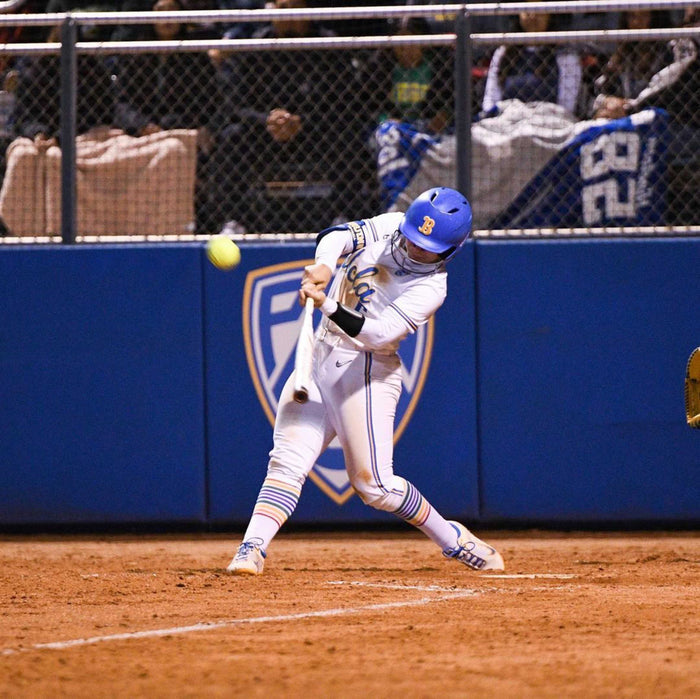softball athlete wearing Warrior rainbow compression pride socks while hitting the softball to make a homerun