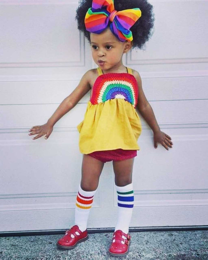 Lifestyle image of Courage rainbow toddler socks with girl with yellow dress on and rainbow headband