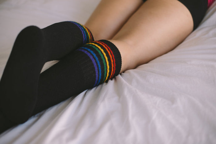 Person wearing black Strength rainbow socks while laying down on the bed